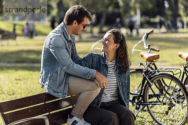 Smiling couple sitting on bench and talking at sunny day