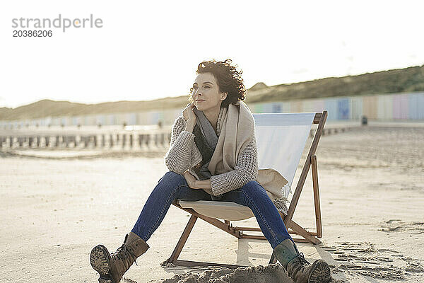 Beautiful woman sitting on deck chair day dreaming at beach