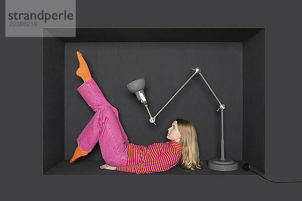 Teenage girl lying in front of electric lamp by black background