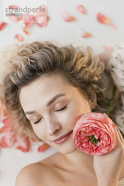 Blond woman with eyes closed holding coral rose Mandarin X-Pression