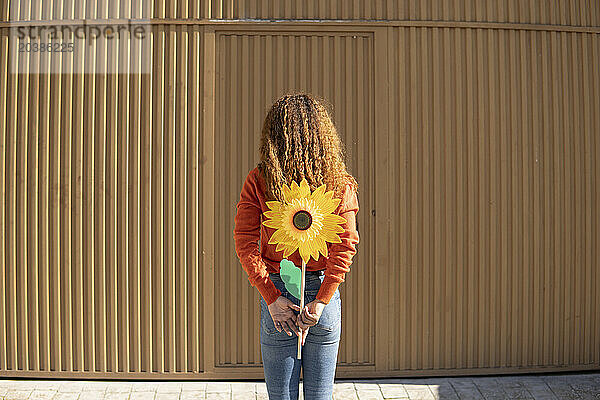 Young woman holding artificial sunflower in front of metal wall