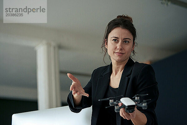 Confident businesswoman holding drone gesturing at home office