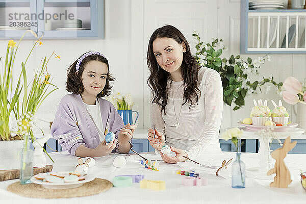 Smiling mother and daughter decorating eggs for Easter at home