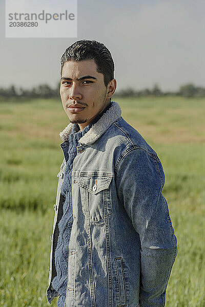 Confident young man in denim jacket standing on meadow