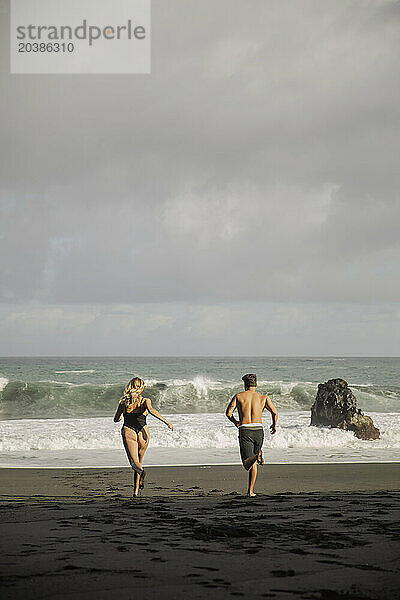 Carefree young couple running towards sea at beach