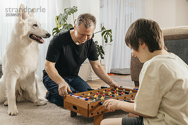 Happy father playing foosball with son near dog at home