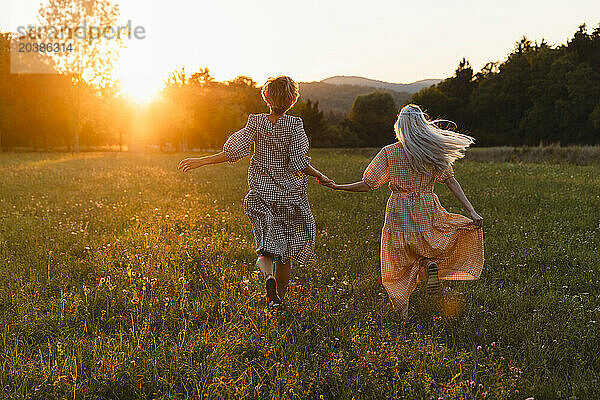 Friends holding hands and running on grass in park