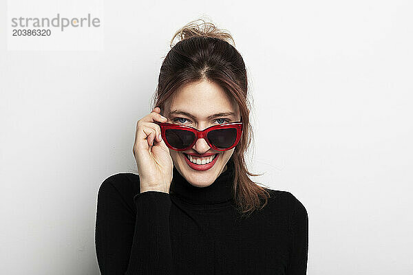 Smiling beautiful young woman wearing sunglasses against white background