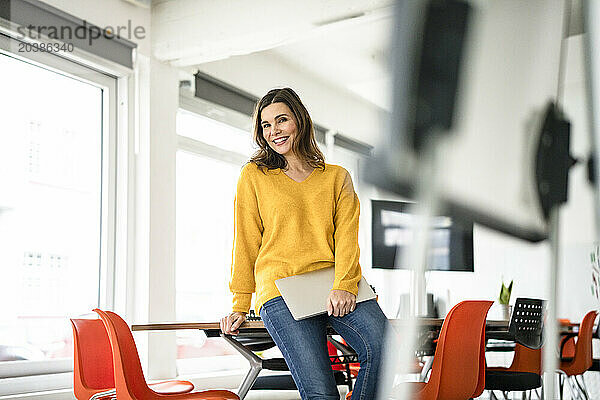 Smiling creative businesswoman with laptop in meeting room