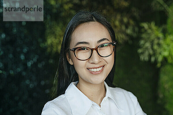 Smiling young businesswoman wearing eyeglasses in front of plants