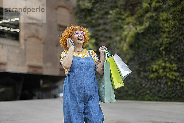 Cheerful woman with shopping bags talking on mobile phone