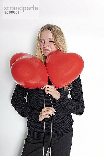 Girl with eyes closed holding balloons standing against white background