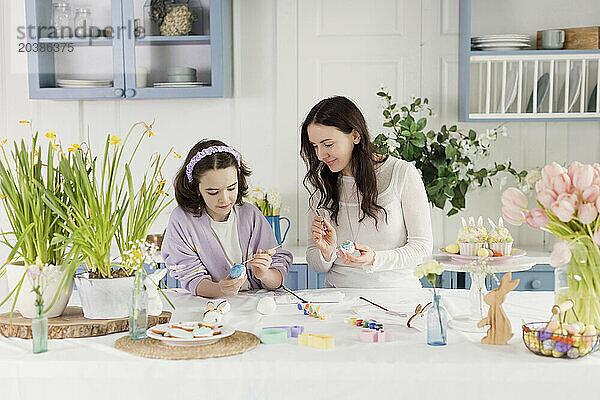 Woman looking at daughter decorating Easter eggs at home