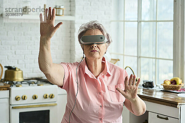 Senior woman wearing VR glasses and gesturing in kitchen at home