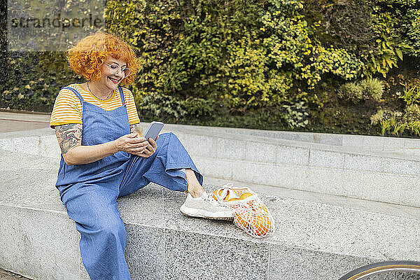 Redhead woman using smart phone sitting on retaining wall