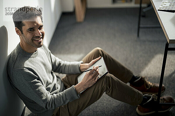 Smiling businessman sitting with tablet PC and digitized pen in office