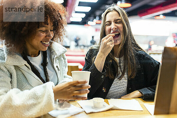 Happy woman having food with friend in cafe