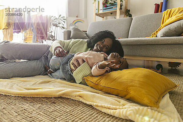 Happy young mother lying with daughter enjoying in living room at home