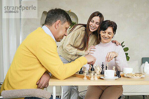 Smiling woman with parents playing chess at home