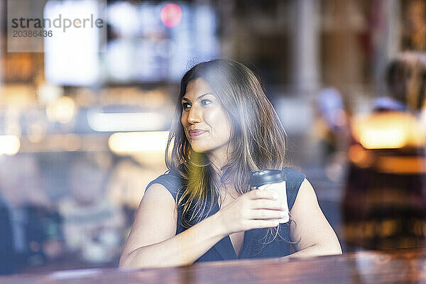 Smiling woman sitting with coffee cup and seen through glass