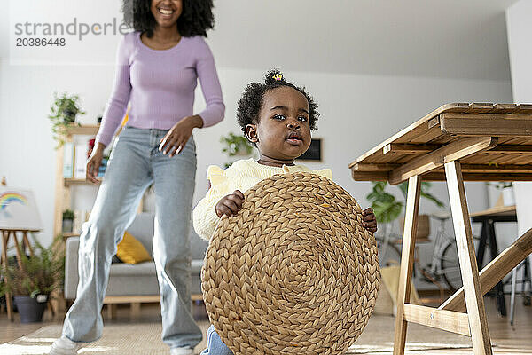 Cute baby girl holding circle shaped place mat with mother in background at home