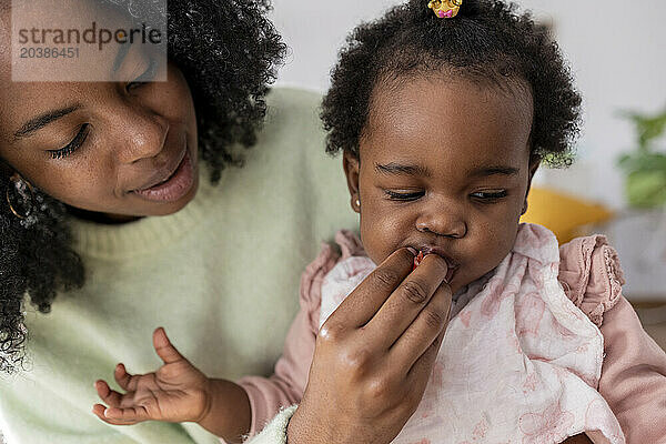 Young mother feeding strawberry to daughter at home