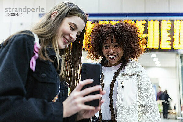 Smiling woman showing smart phone to friend at railroad station