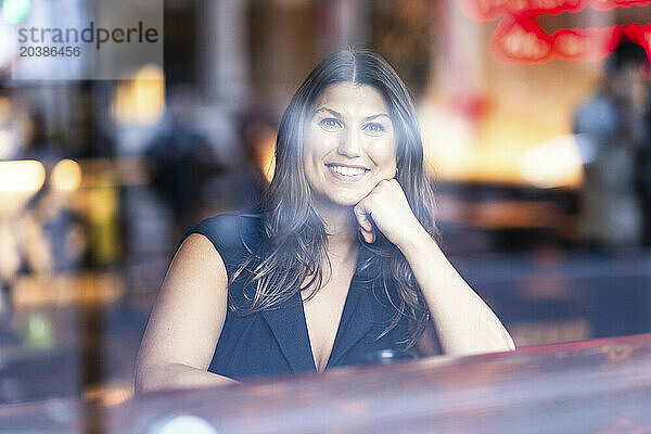 Happy woman sitting in cafe seen through glass