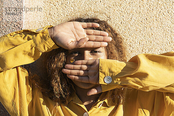 Curly haired woman looking through hands on sunny day