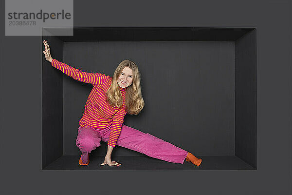 Smiling blond teenage girl stretching against black background