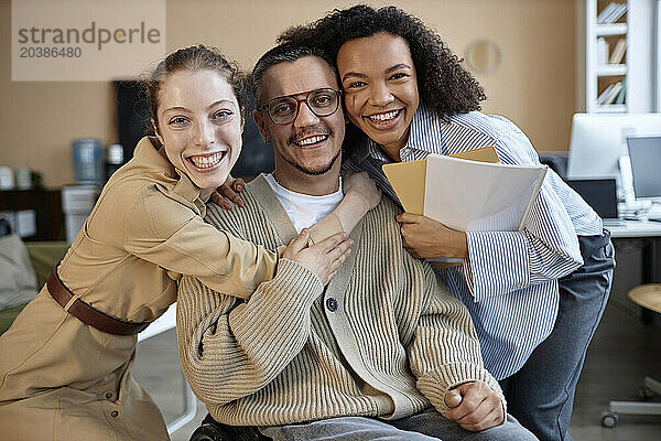 Cheerful businesswomen hugging colleague with disability in office