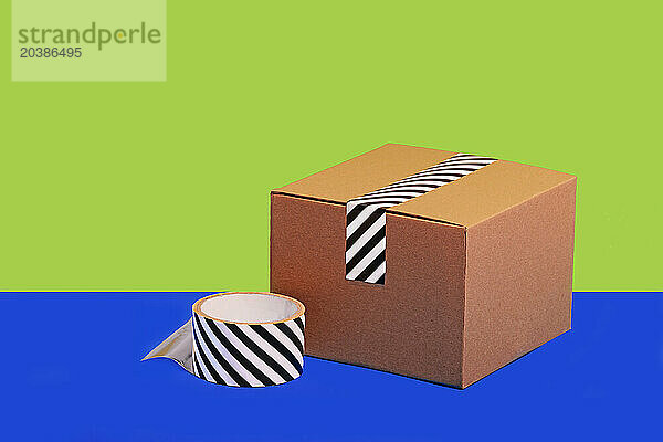 Striped adhesive tape and cardboard box against green and blue background