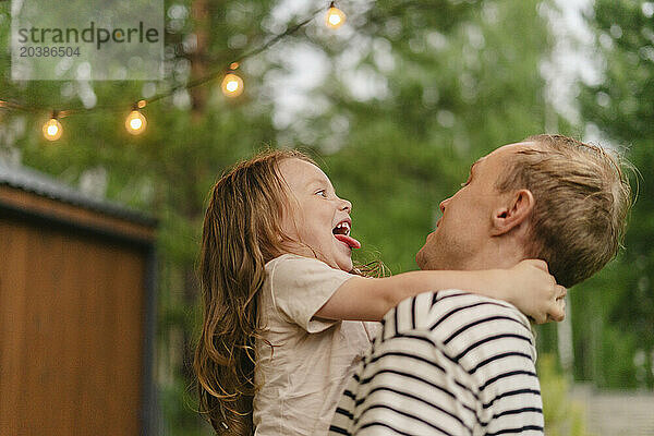 Playful father carrying happy daughter in back yard