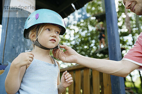 Father fastening helmet of daughter at rope park