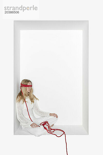 Teenage girl with thread tied on eyes sitting in alcove