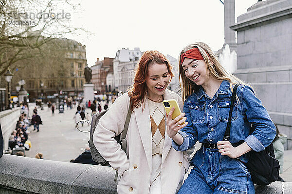 Happy woman with friend using smart phone in city of London