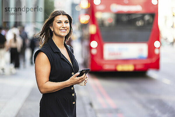 Smiling young woman standing with smart phone at street