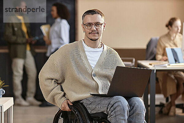 Smiling businessman sitting with laptop in wheelchair at office