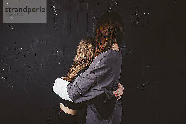 Girls embracing in front of black background