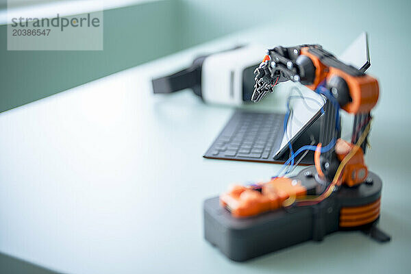 Robotic arm near tablet PC and virtual reality simulator on desk