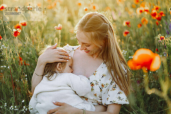 Smiling mother breastfeeding daughter in flower field