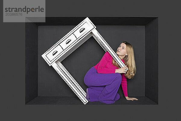 Blond teenage girl with table in alcove against black background