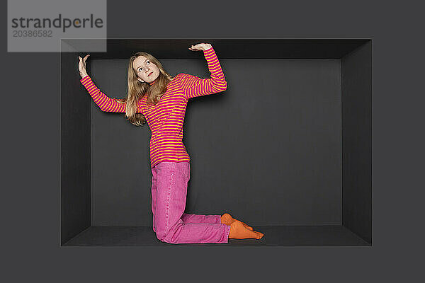 Teenage girl kneeling in alcove against black background