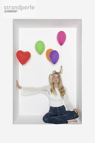 Teenager with multi colored balloons sitting in alcove