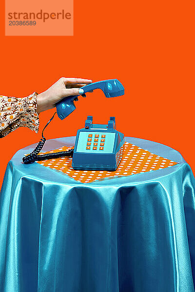 Woman holding telephone receiver on table against orange background