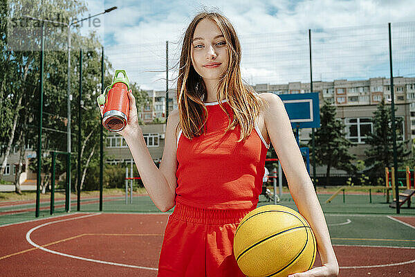 Teenage basketball player holding water bottle in school yard