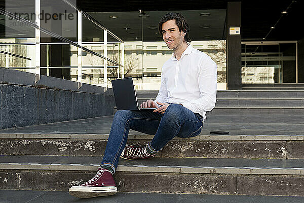 Smiling businessman with laptop sitting on steps