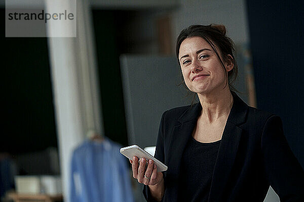 Smiling beautiful businesswoman standing with smart phone at home office