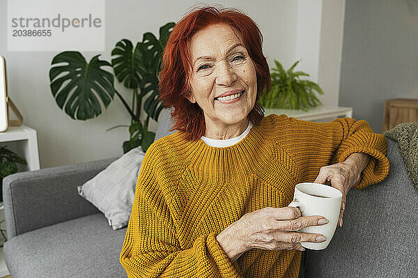 Happy woman holding tea cup sitting on sofa at home