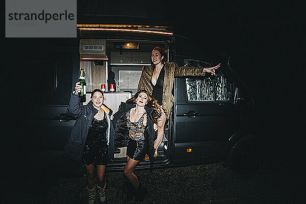 Happy women celebrating New Year's eve with champagne bottle outside motor home at night